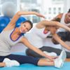 Women doing stretching exercises as trainer helps one