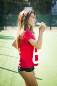 Happy beautiful young woman eating a banana on the playground